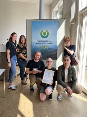 Sechs Personen mit Urkunde vor Plakatwand